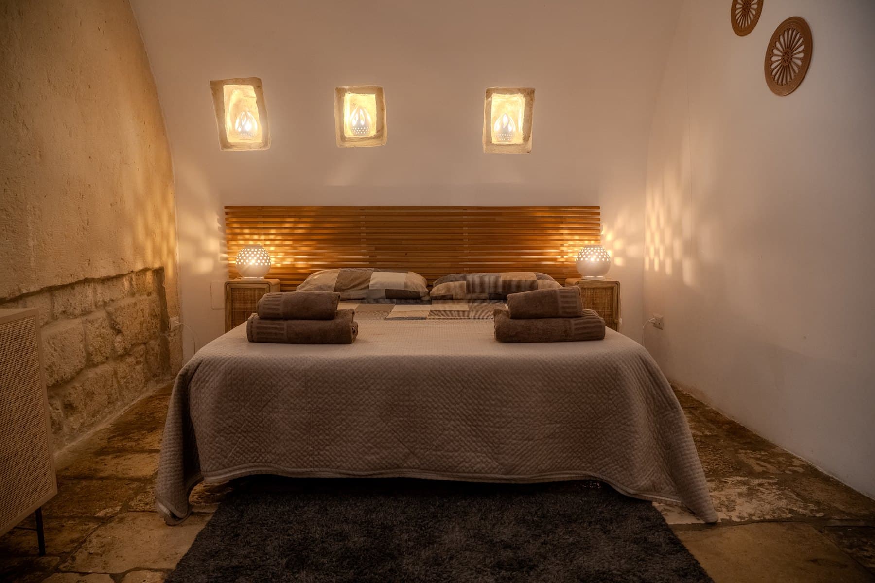 Il letto matrimoniale con testiera in legno a doghe e le tre nicchie luminose ricavate nella volta