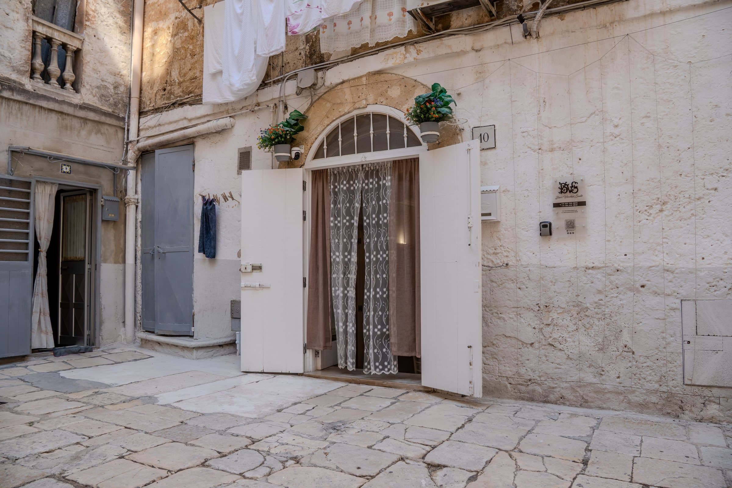 La corte del centro storico con il portone numero 10 aperto, i panni stesi in alto e il basolato in chianche