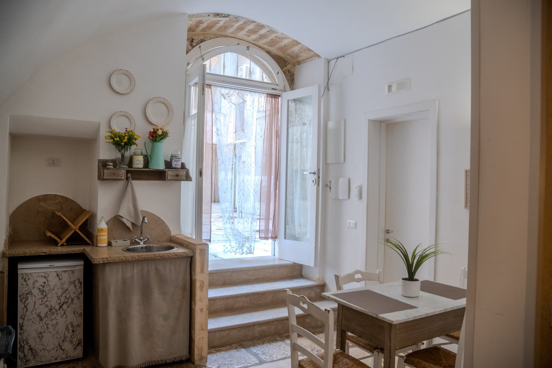 L’angolo cottura in pietra e la porta ad arco che sale verso la corte, con la luce che entra dai vetri