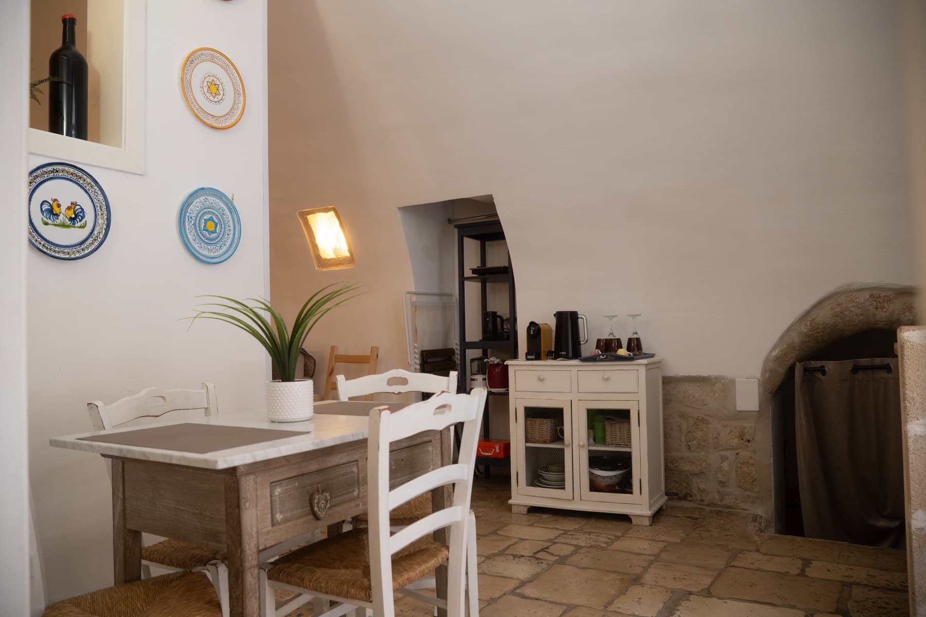 La zona pranzo con i piatti in ceramica decorata al muro e la nicchia ad arco in pietra